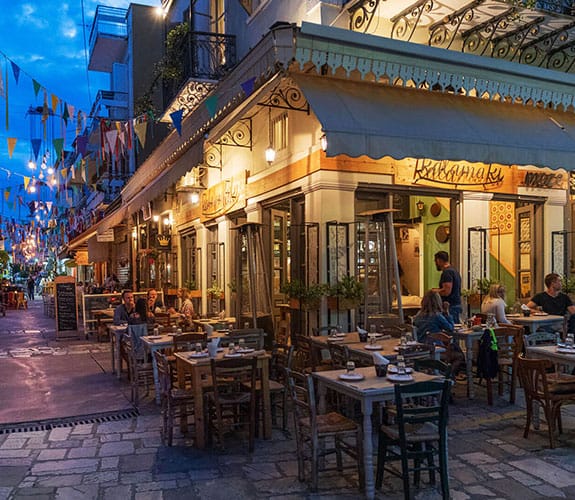 Lively pedestrian street in Kalamata with tavernas and festive flags at dusk